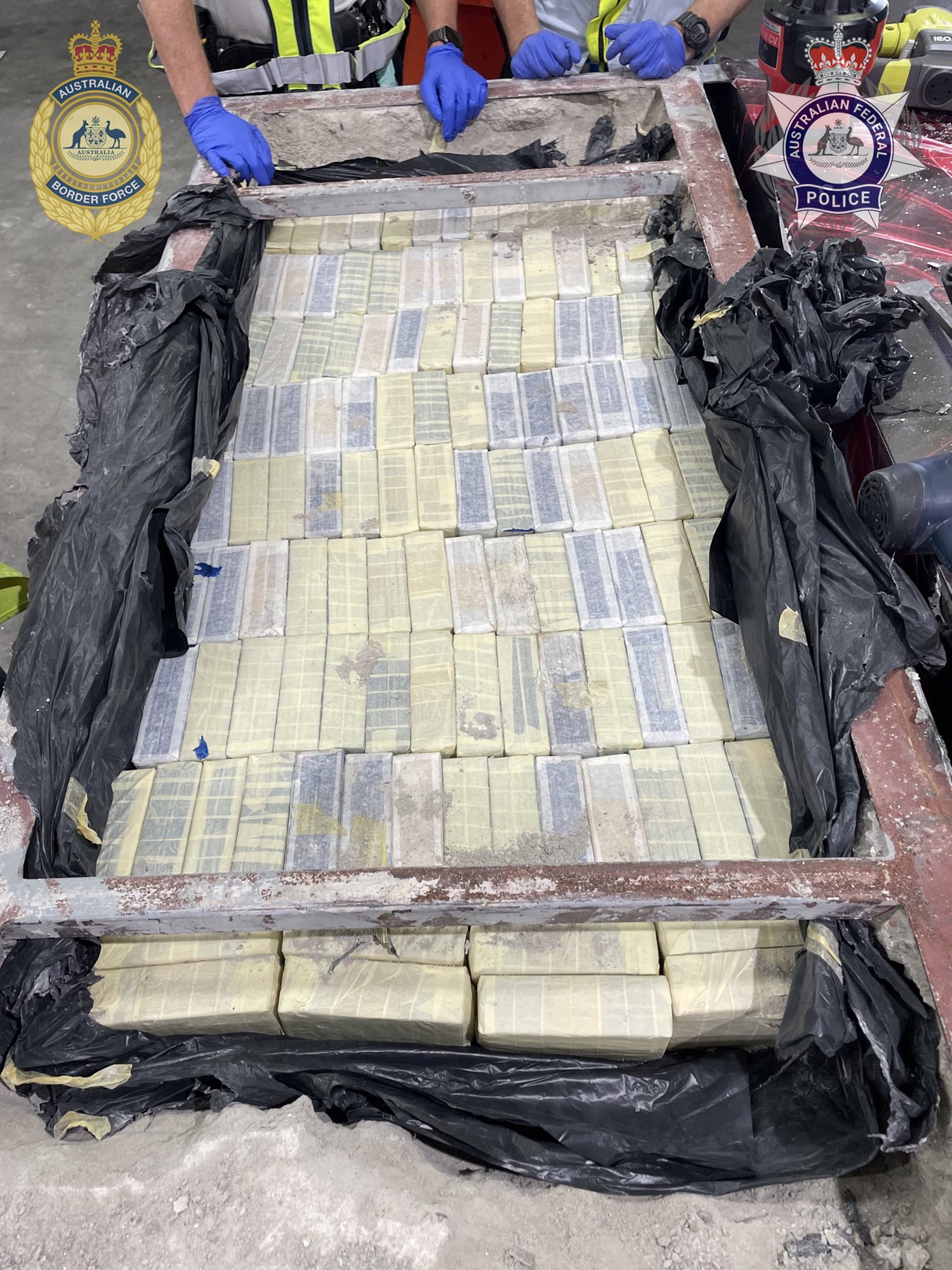 A police-supplied photo of tightly wrapped packets of heroin lying in inside a concrete block. Officers wearing gloves stand behind it