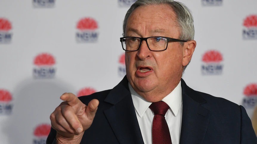 A man wearing a suit points while standing in front of a media wall.