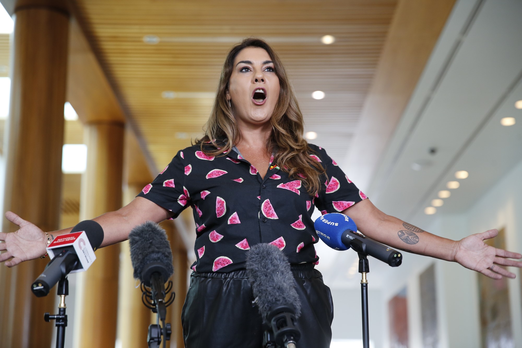 Jacinta Price with her arms spread out in front of microphones. 