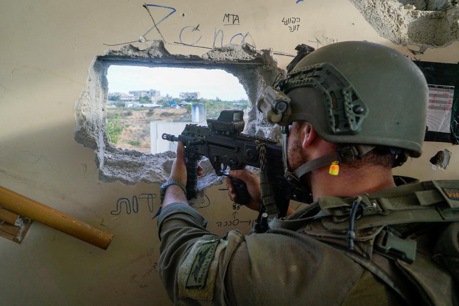 A soldier pointing a gun through a hole in a wall. 