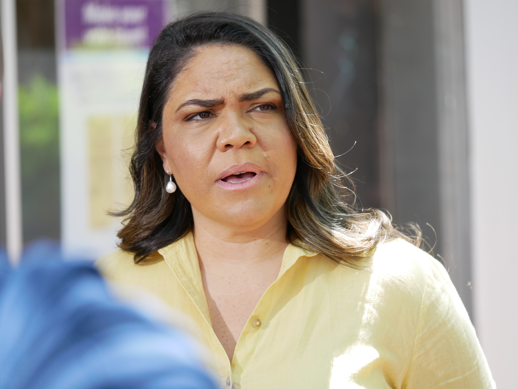 A close up of Jacinta speaking in a pale yellow blouse.