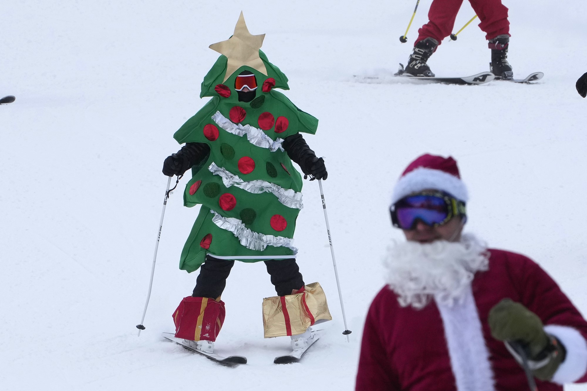 A person in a Christmas tree costume skis downhill.