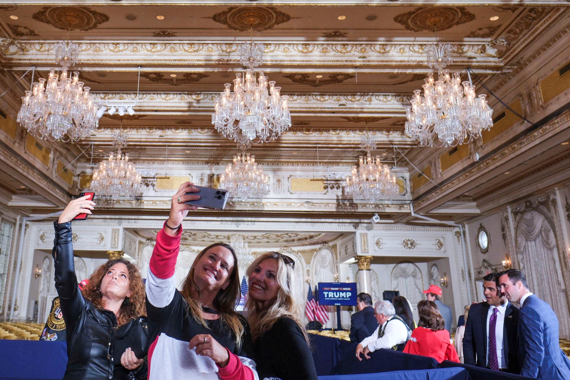 Three women take selfies in a ballroom.
