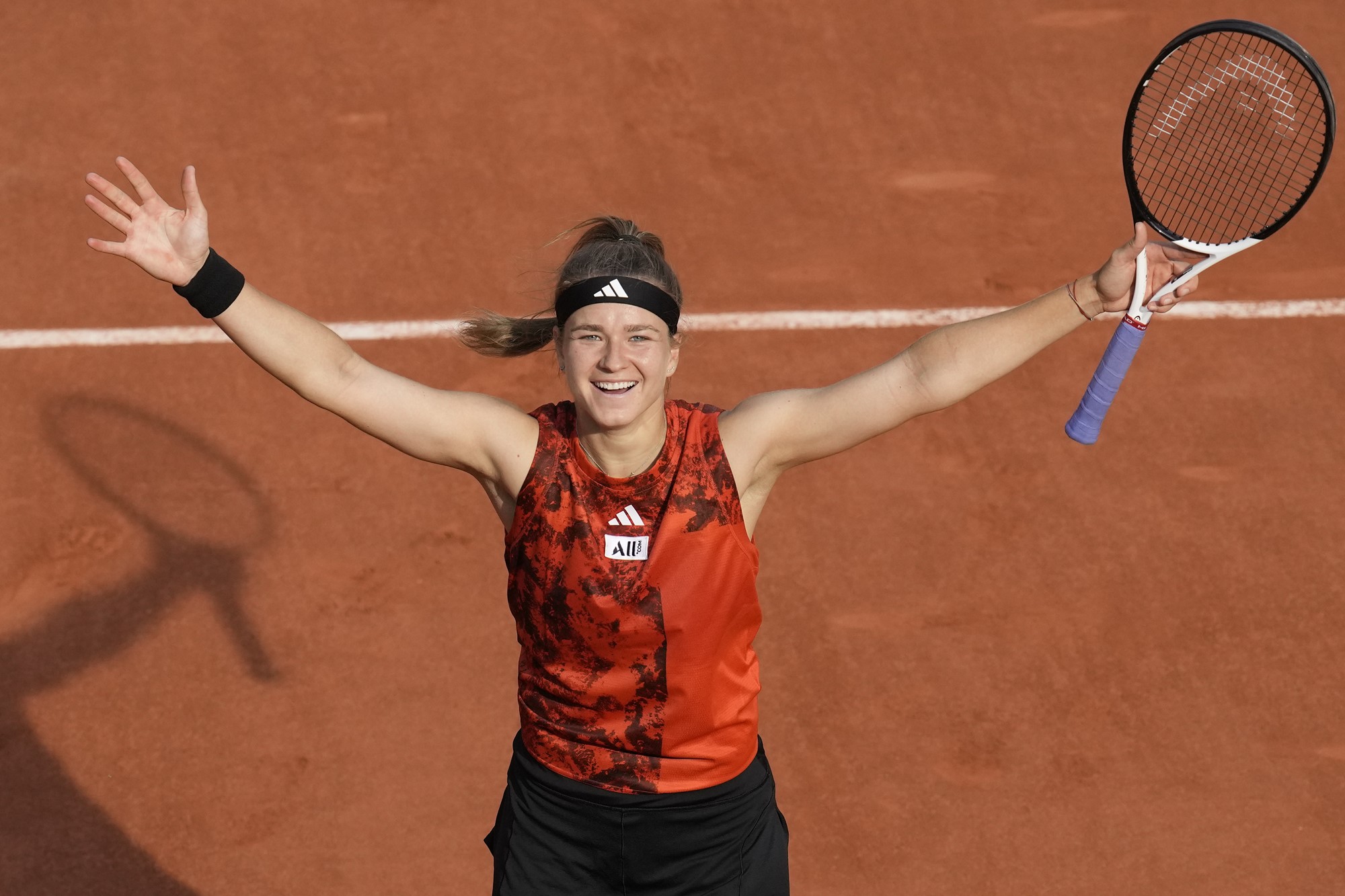 A female tennis player in red raises her arms in celebration on a clay court