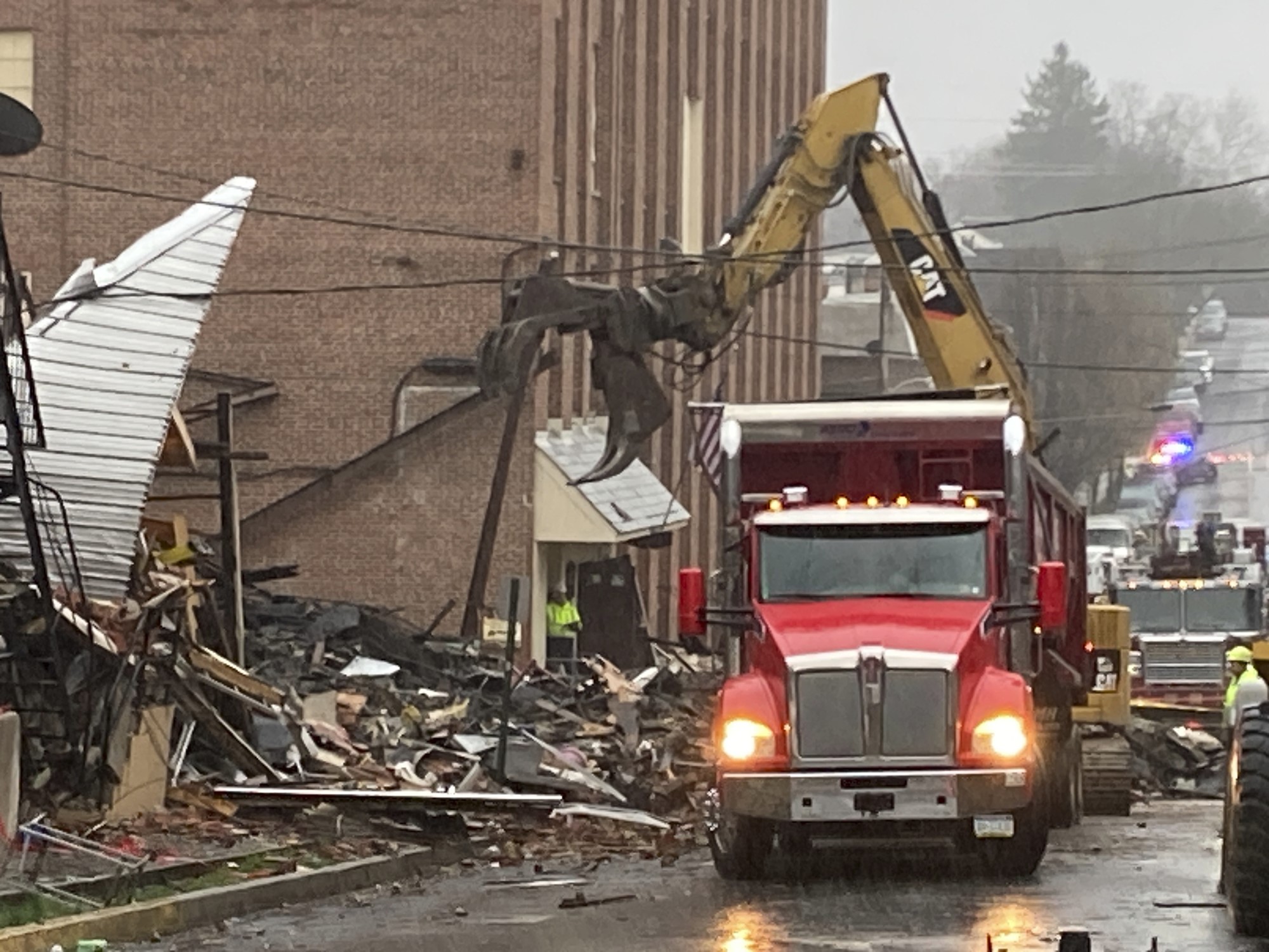 A truck is used to clear debris next to a damaged building. 