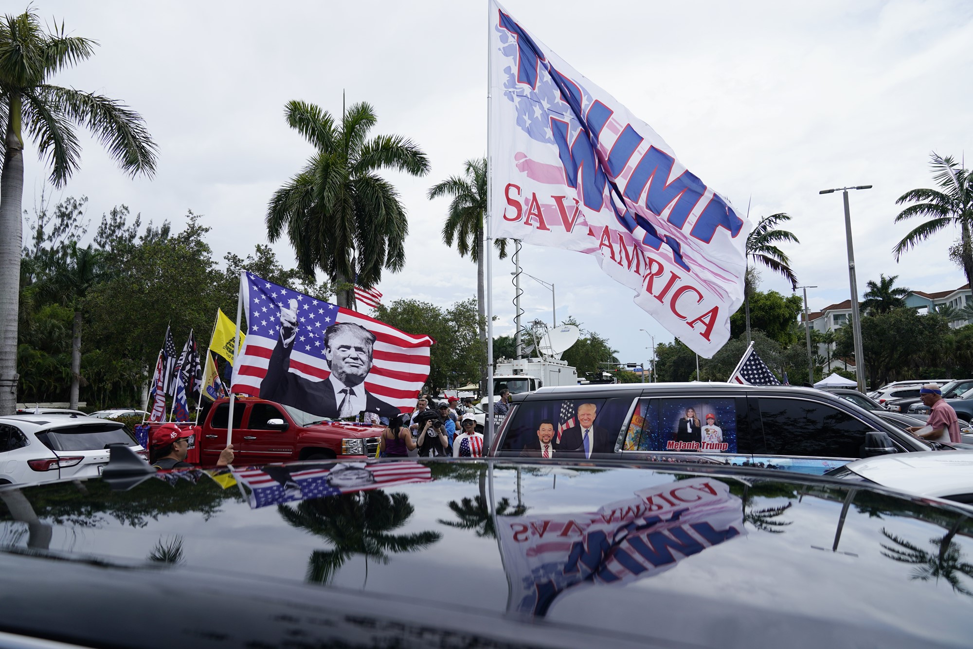 Flags displaying Donald Trump and the American flag held over large SUVs, with people nearby