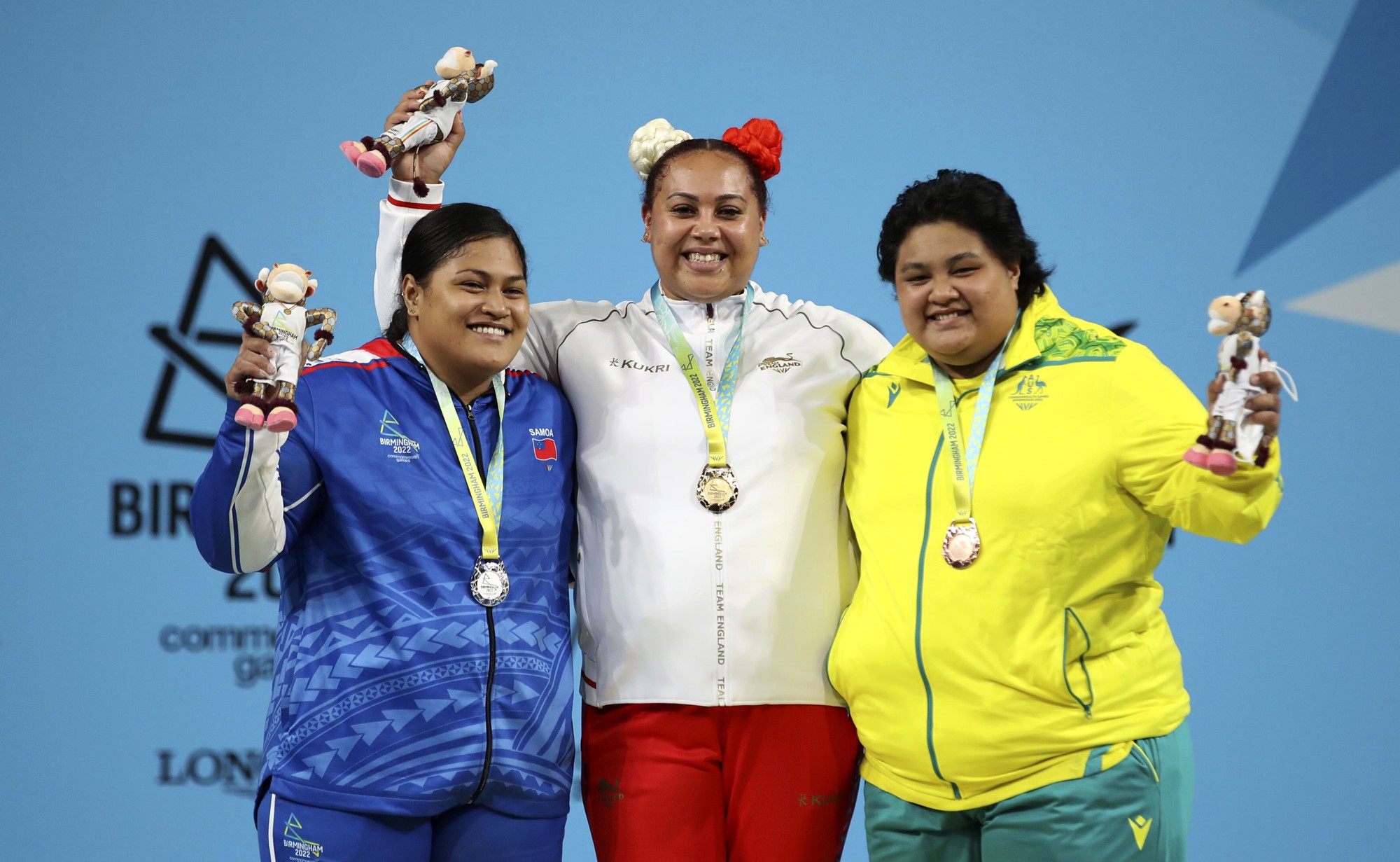 Three women smile for the camera on the podium for weightlifting at the Commonwealth Games.