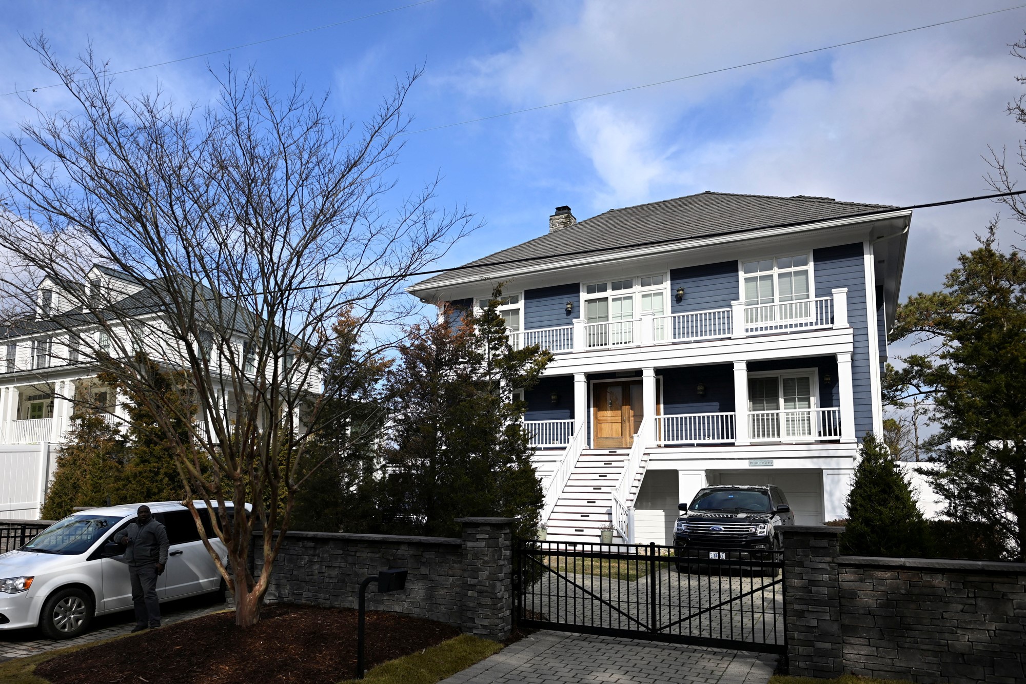 A two-story beach house with navy shiplab and white balastrades with security guards standing outside.