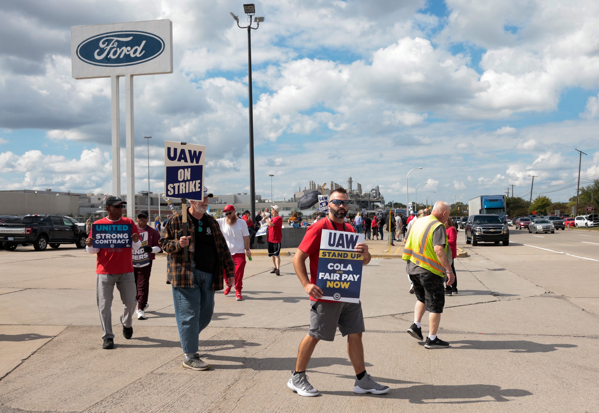 People holding protest signs outside a Ford car manufacturing plant.