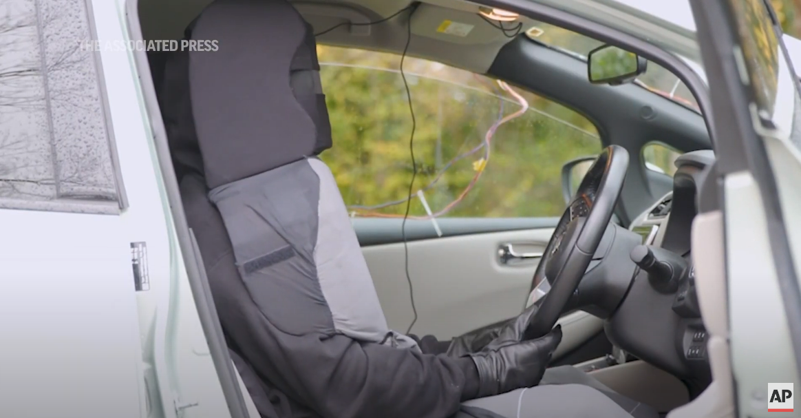 A man disguised as a car seat, sitting in a car