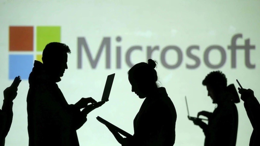 Silhouettes of people on their laptops in front of a giant Microsoft logo