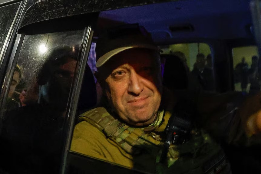 Yevgeny Prigozhin smiles through an open car window, he is wearing military uniform