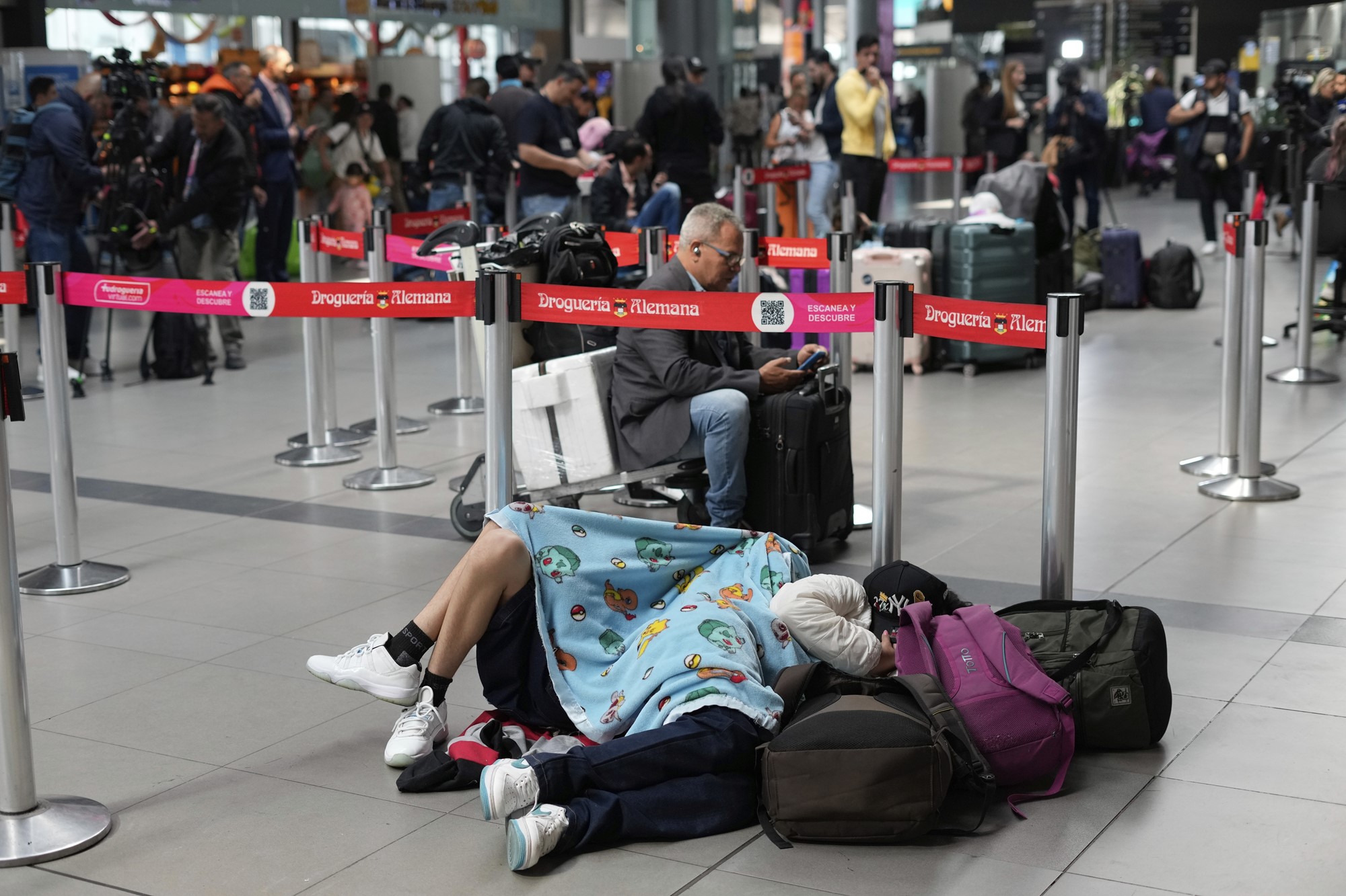 Passengers sleep on the ground in front of an airport queue. 