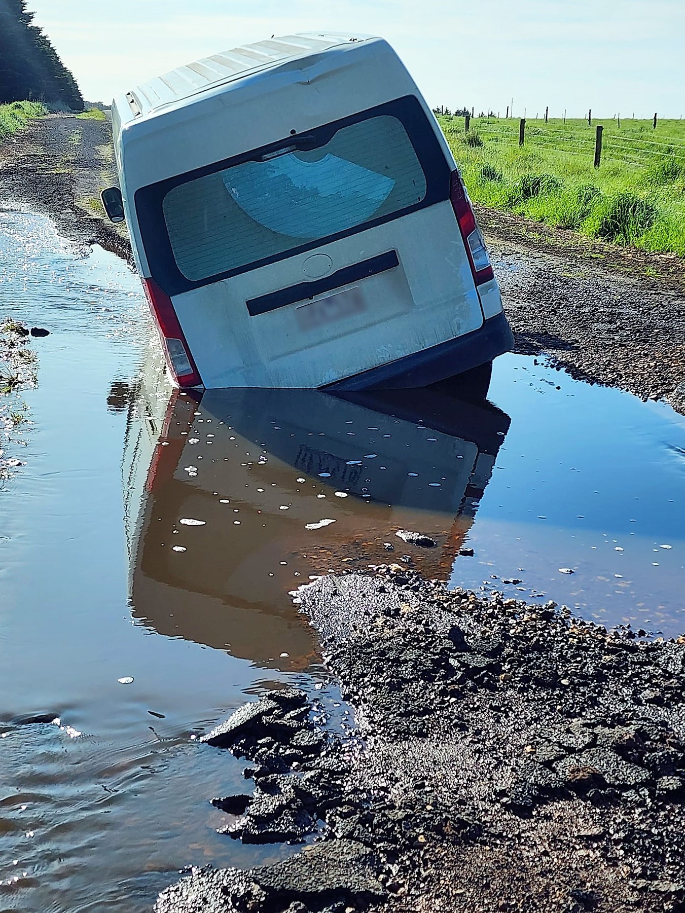 A van became is stranded in floodwater next to a field.