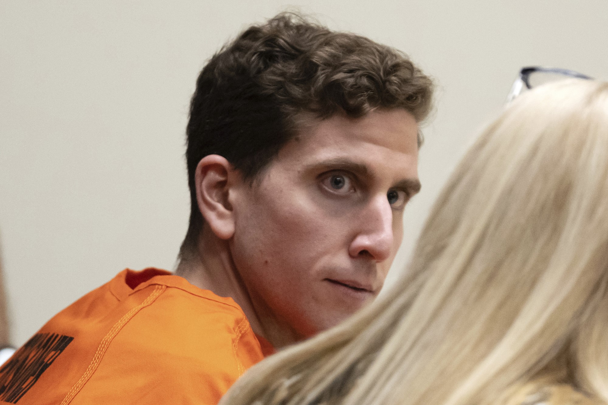 Brian Kohberger in orange jumpsuit looks toward a woman with blond hair. 