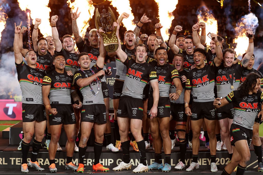 Penrith Panthers hold up the NRL premiership trophy as flames fly behind them.