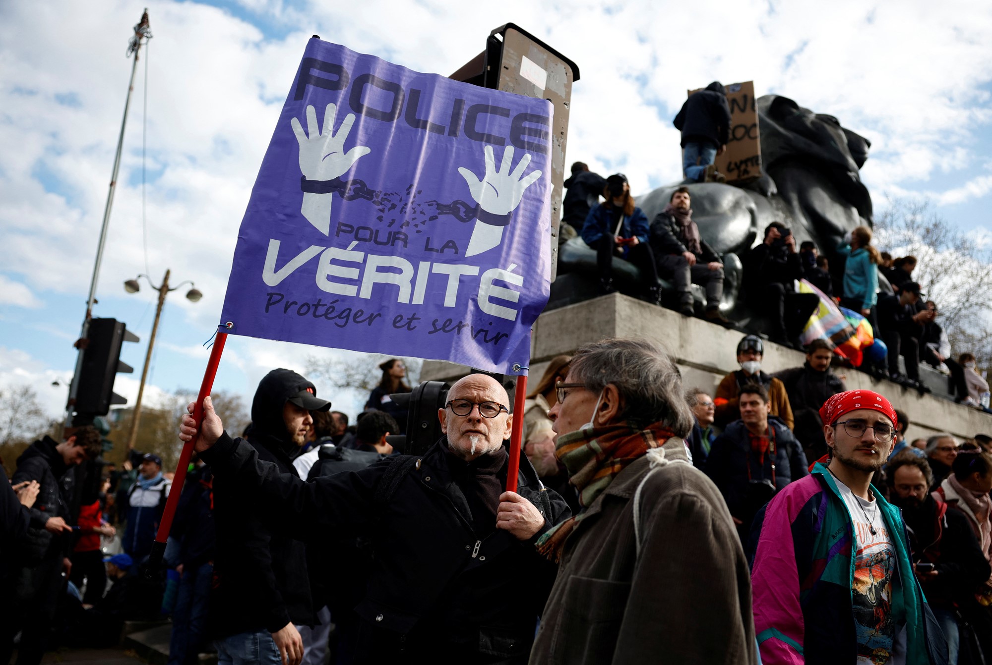 A person amid a protest crowds holds a blue anti-police sign in French. 