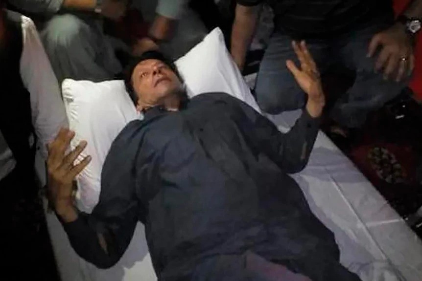 Imran Khan lying on a bed with his hands up.