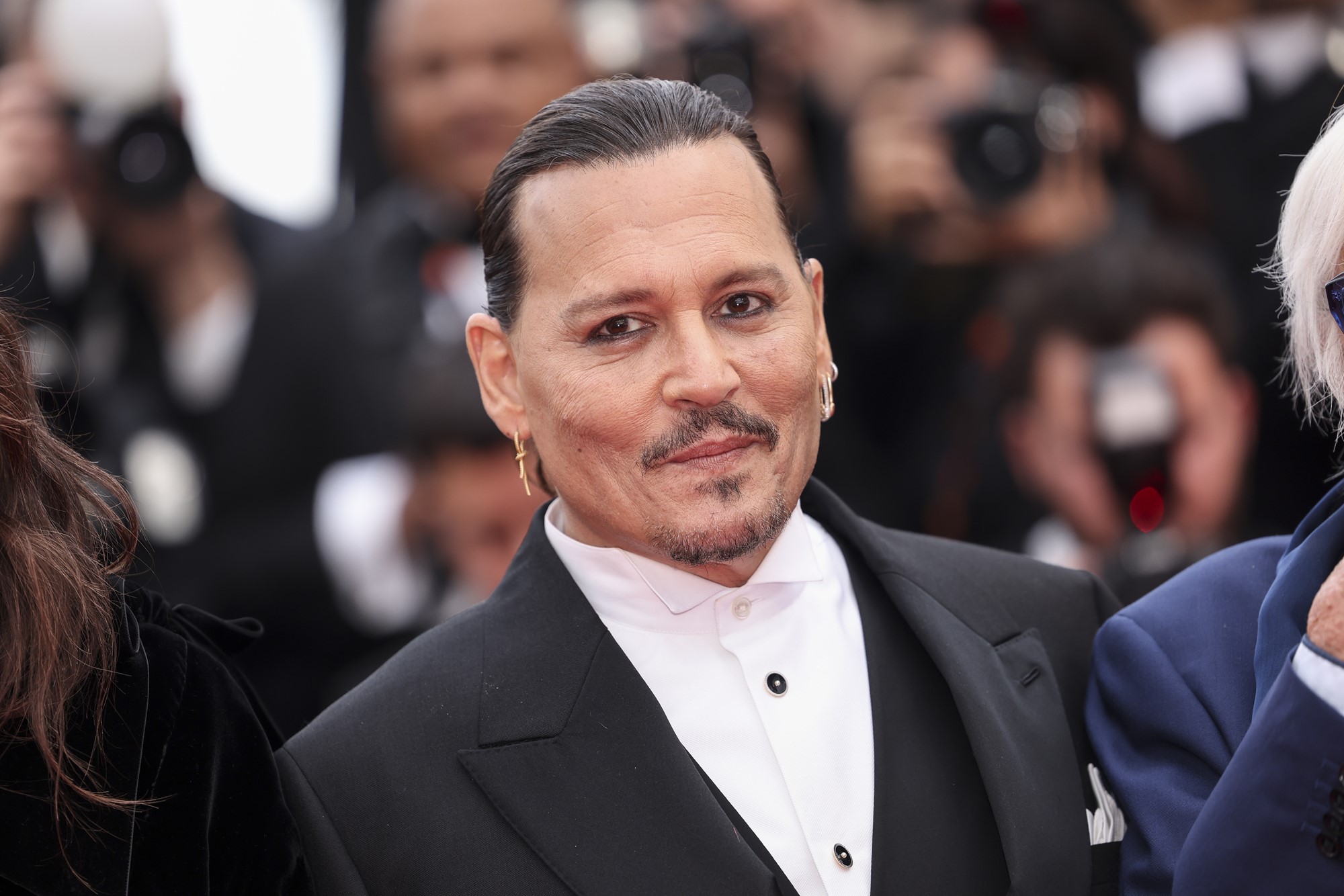 Actor Johnny Depp in a suit and collared shirt, smiling without teeth with photographers behind him
