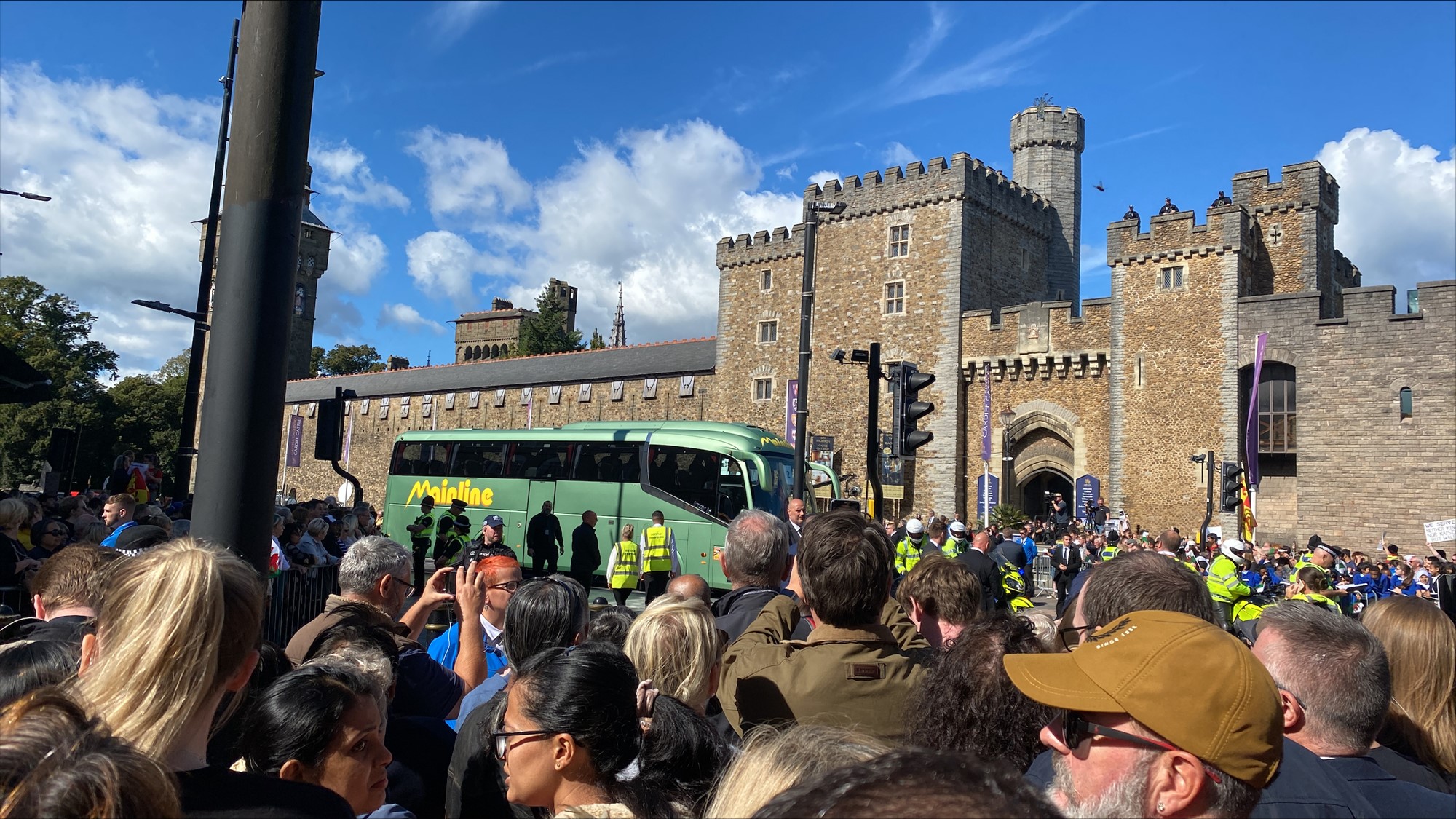 Crowds of people stand in front of an old castle on a sunny day.