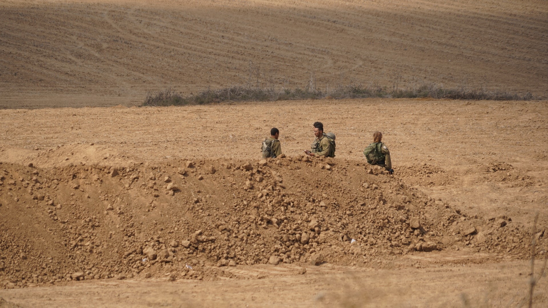 Three men stand around behind a pile of dirt.