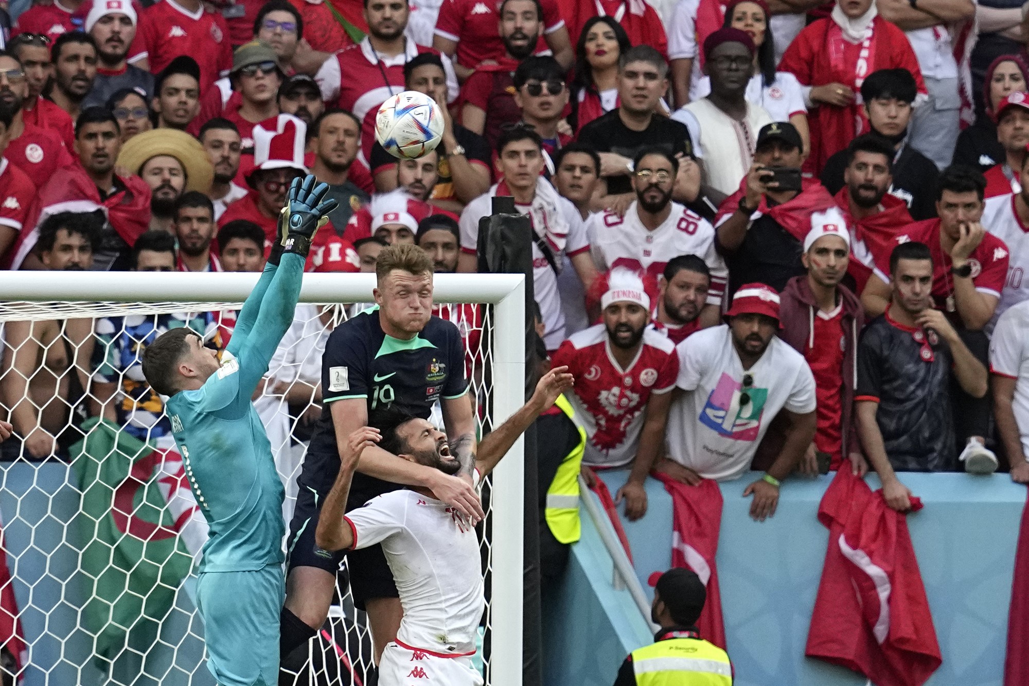 An Australian goalkeeper and defender go up for the ball in a physical contest with a Tunisian forward.