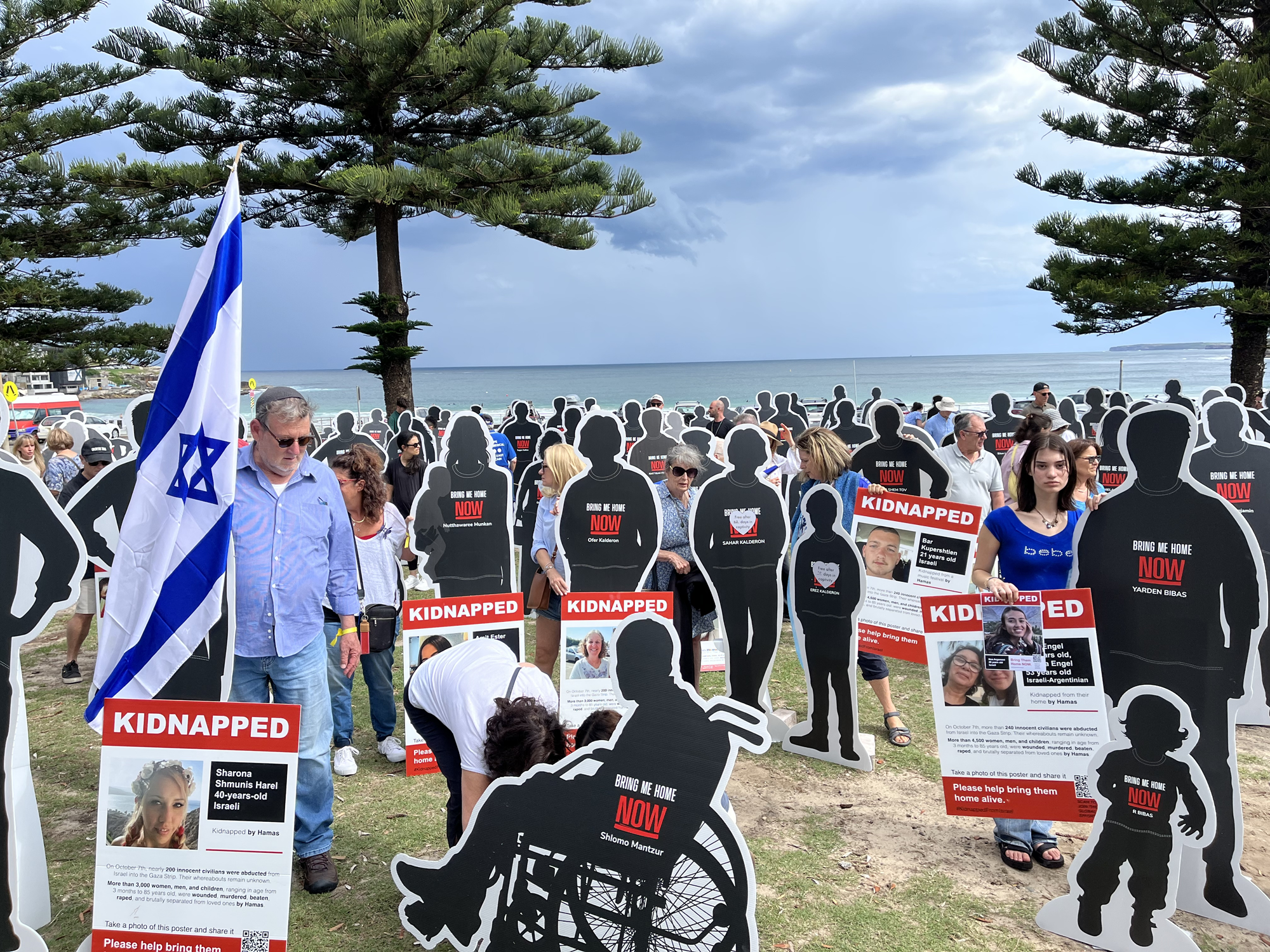 People standing around cutouts of people at a beach holding Israel flags. 