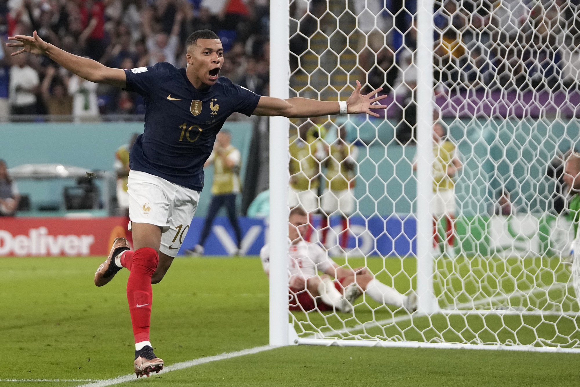French striker Kylian Mbappe runs away from goal with his mouth open and his arms spread wide in celebration after a goal.