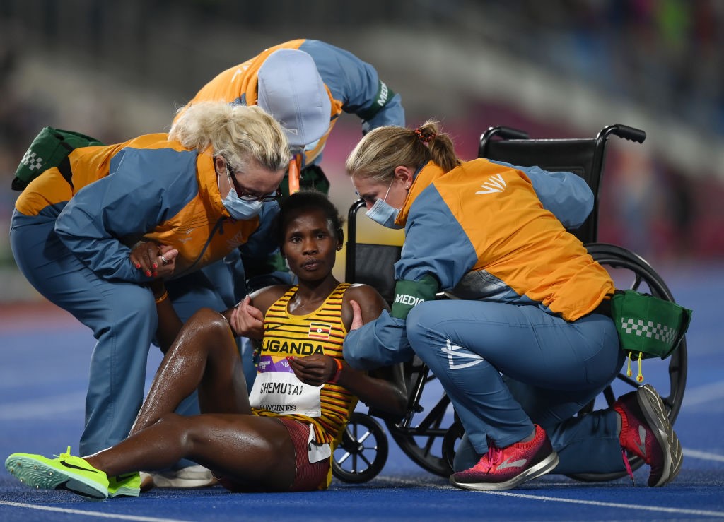 A woman sits on the ground in front of a wheelchair as three people crowd around her