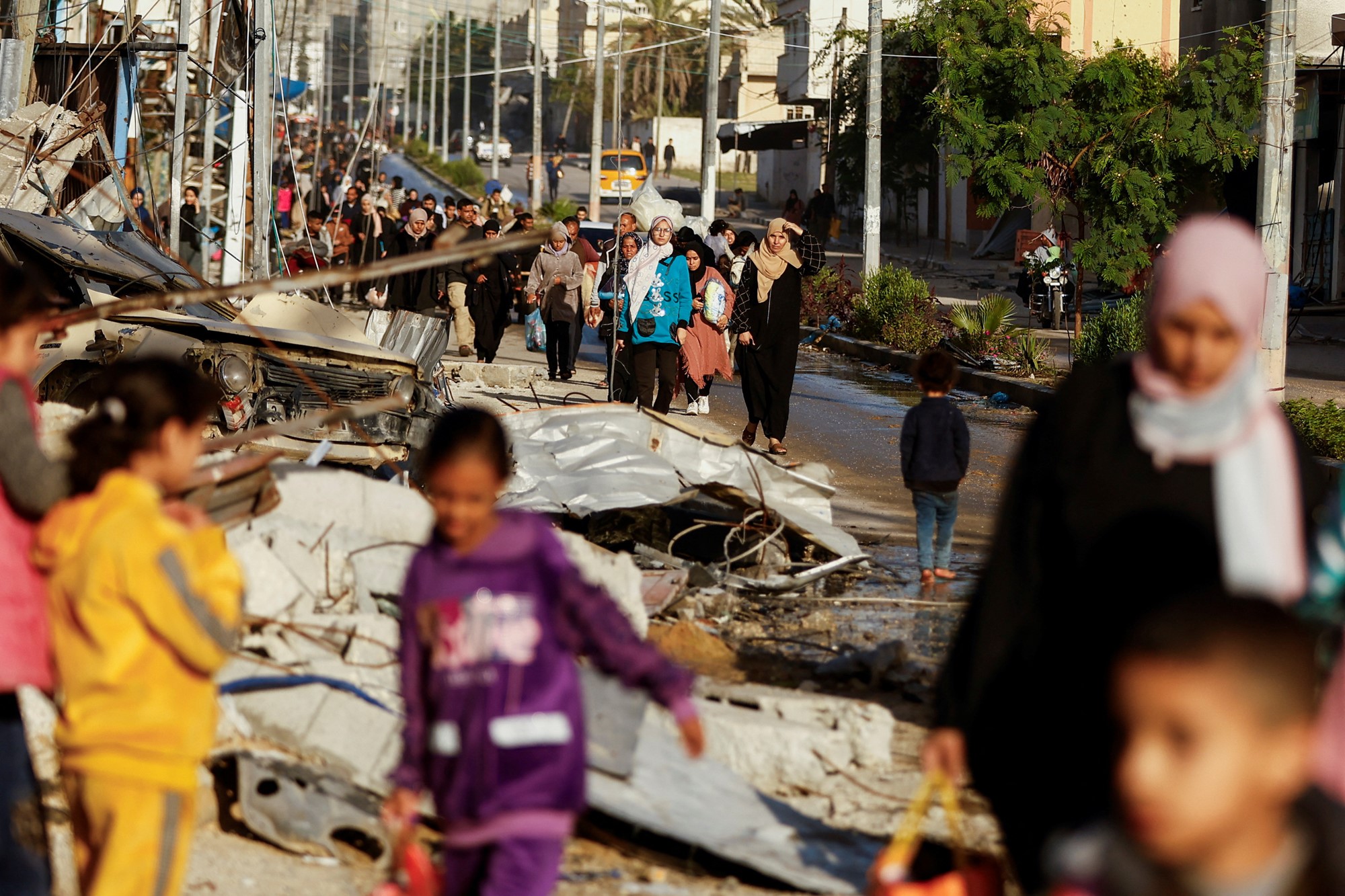 Palestinians are pictured walking through a street with a lot of damage.