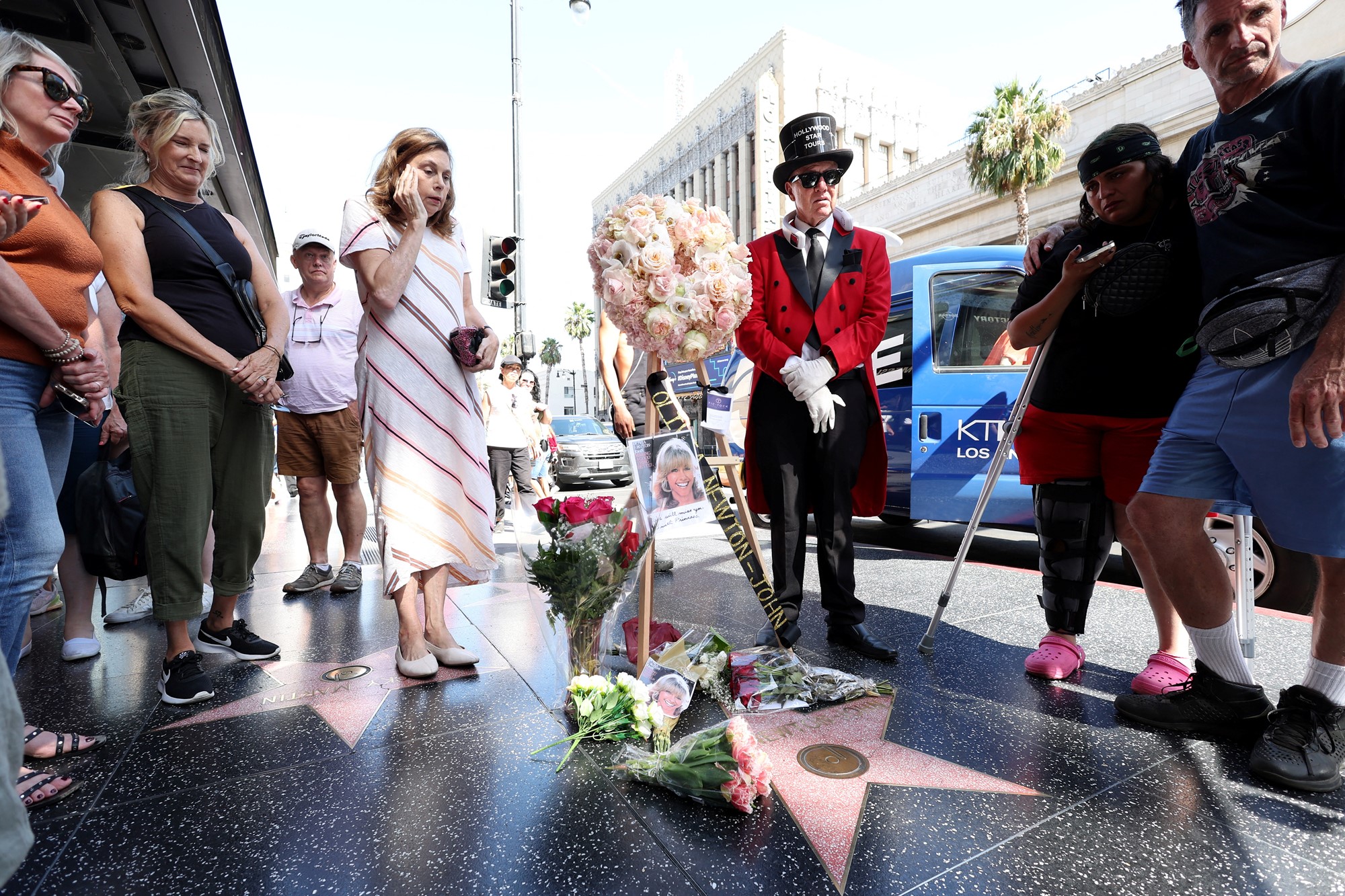 A mourner stands next to a tribute to Olivia Newton-John.
