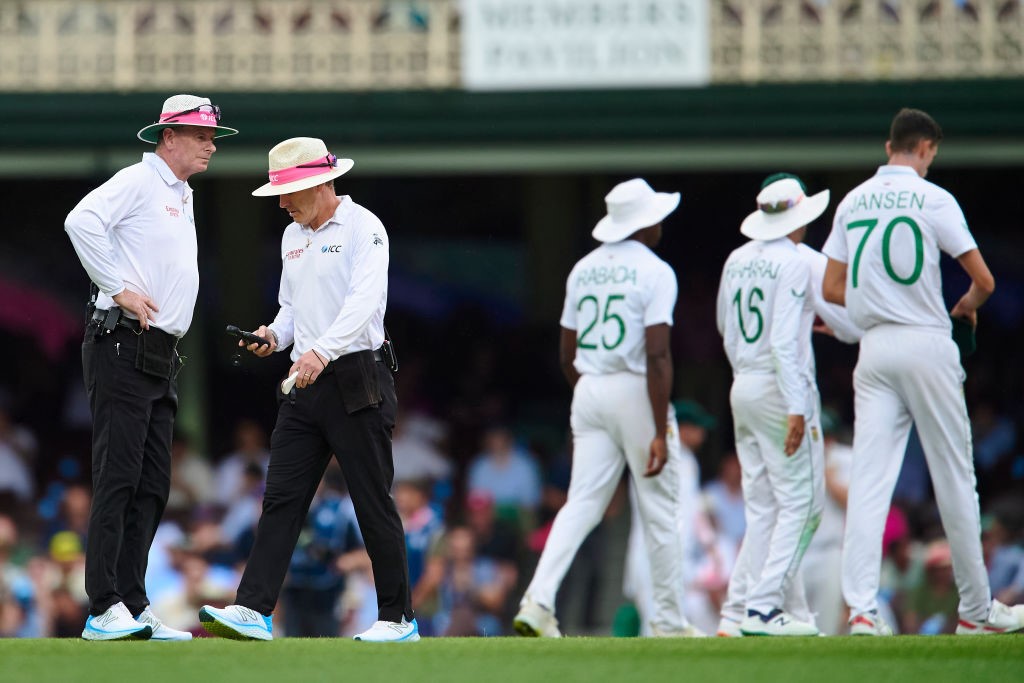 Umpires Chris Gaffaney and Paul Reiffel look at a light meter as South African players walk off the field at the SCG during a Test against Australia.