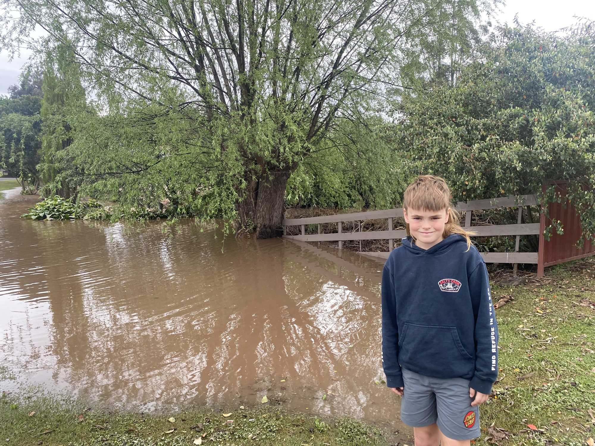 A boy smiles in front of a flooded property.