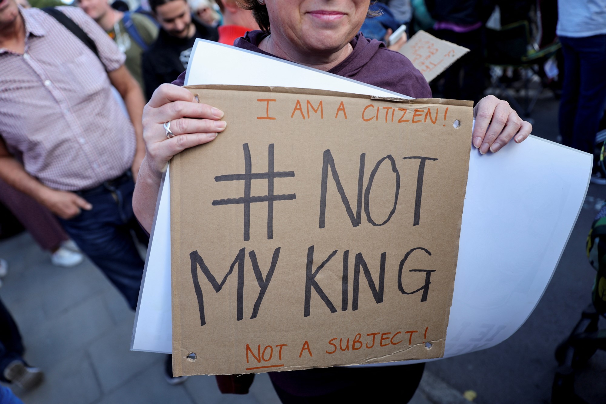 A person holds a cardboard sign that reads "#Not My King".