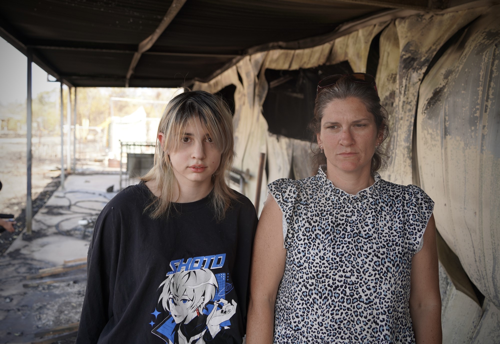 a teenager and her mother stand among the wreckage of their home which has been destroyed by fire