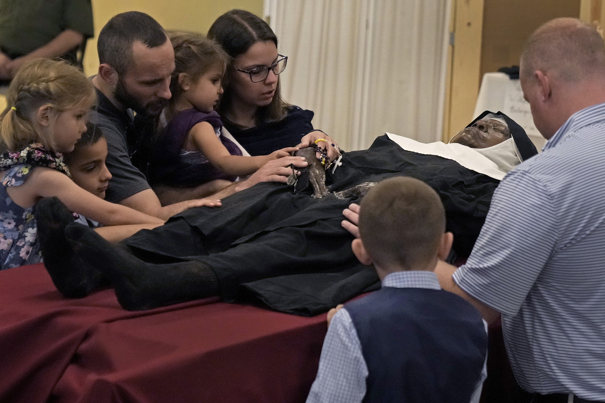 A black nun's body lies in state, with other people's hands touching her and holding rosary beads