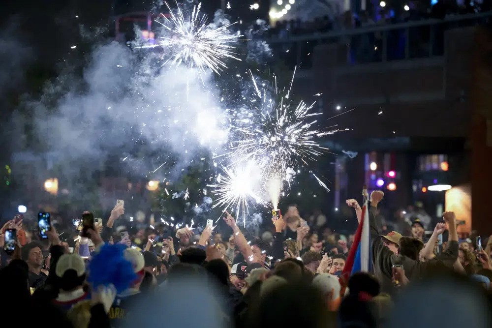 A crowd outside at night, with some people holding up phones and sparklers
