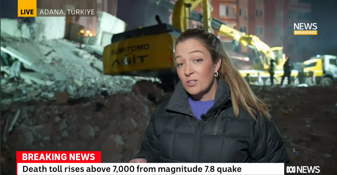 A female news reporter reporting from Türkiye, in front of a destroyed building