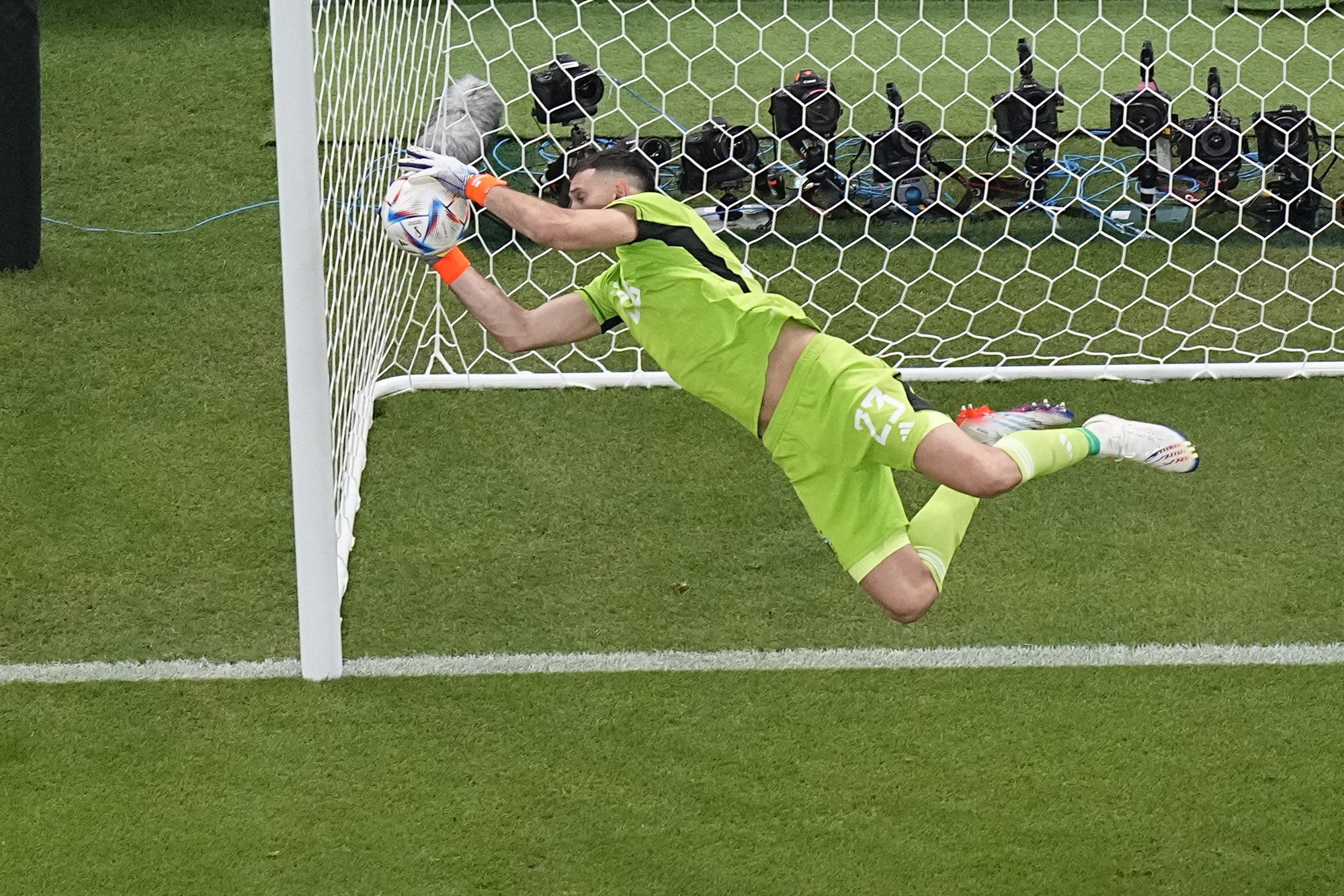 An Argentinian goalkeeper dives to his right to grab the ball near the corner of the net.