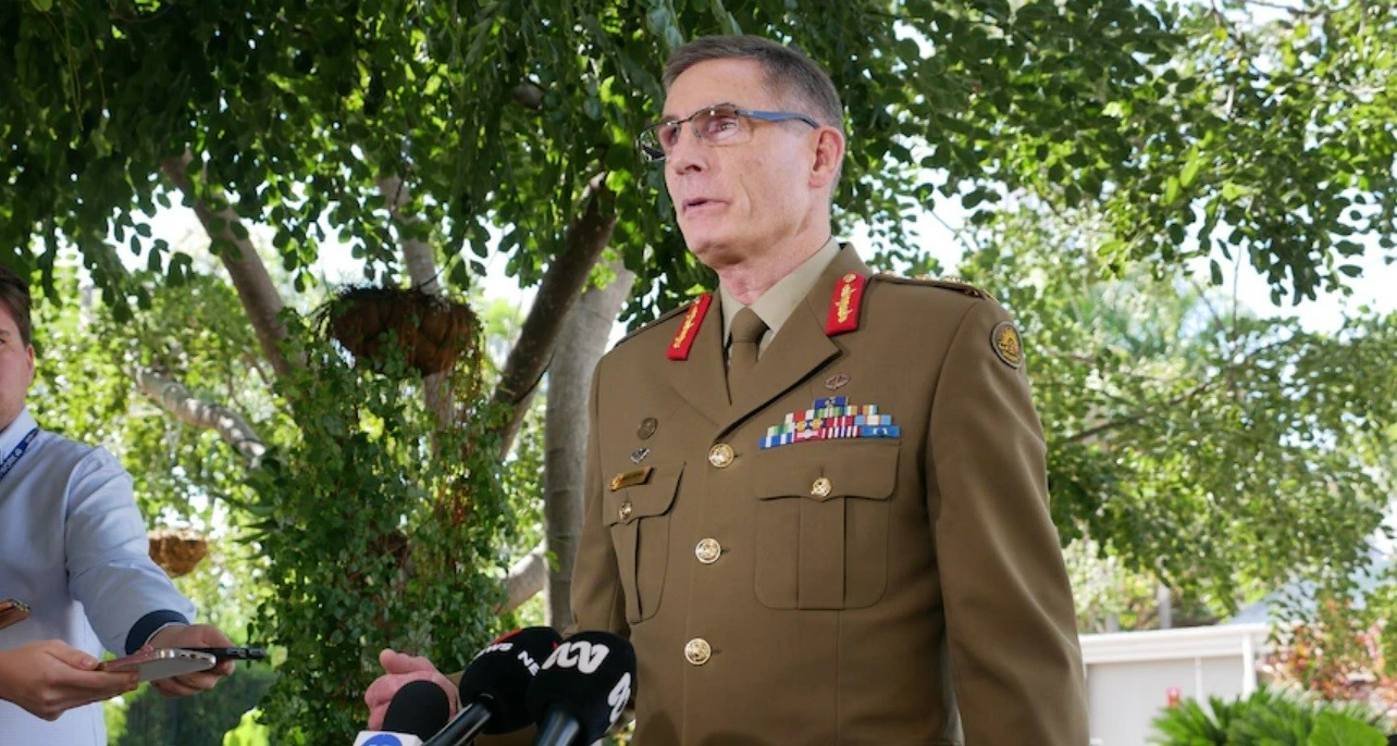 A man in an Australian Defence Force uniform and glasses stands behind microphones at a press conference.