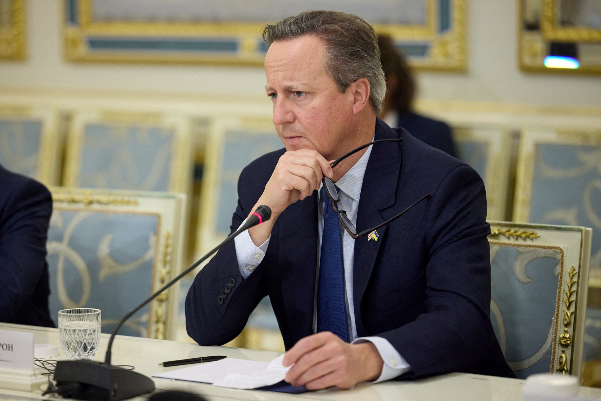 David Cameron sits in front of a microphone with a thoughtful expression