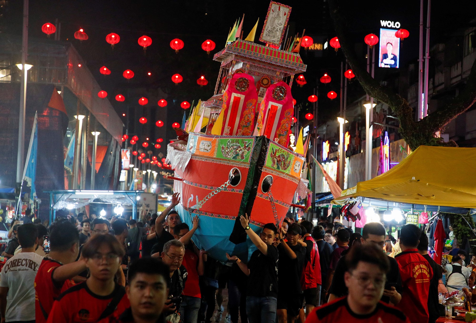 People carry a large colourful boat through a crowded steet