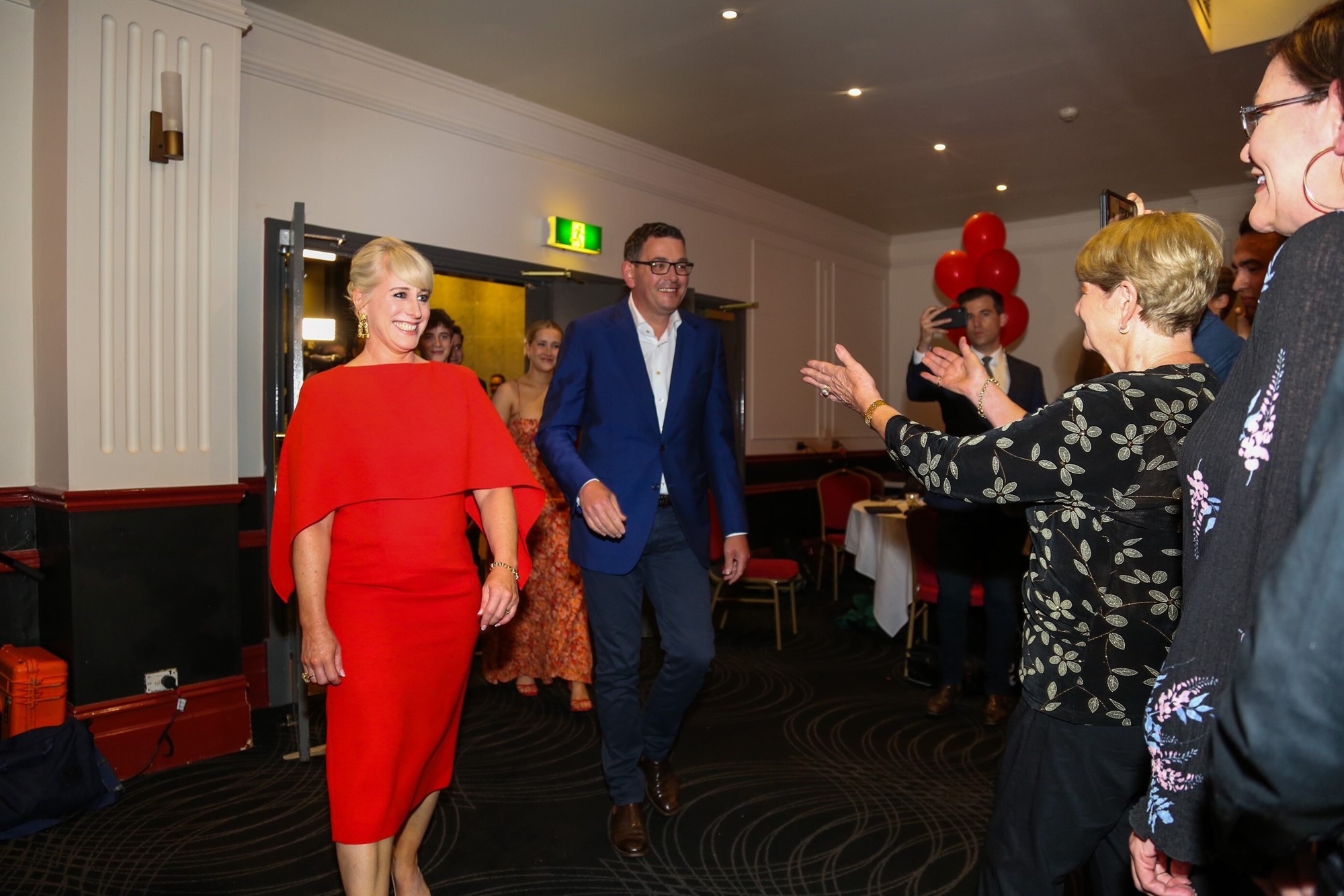 Dan Andrews walks into a room with his wife, who is wearing red.