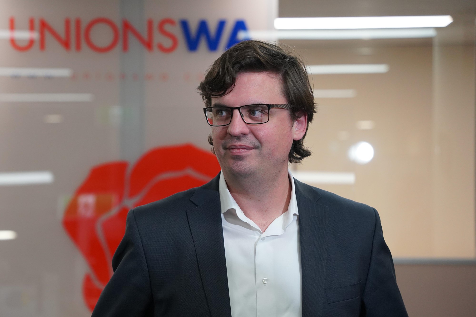 Unions WA secretary Owen Whittle looking to the right in front of a Unions WA sign