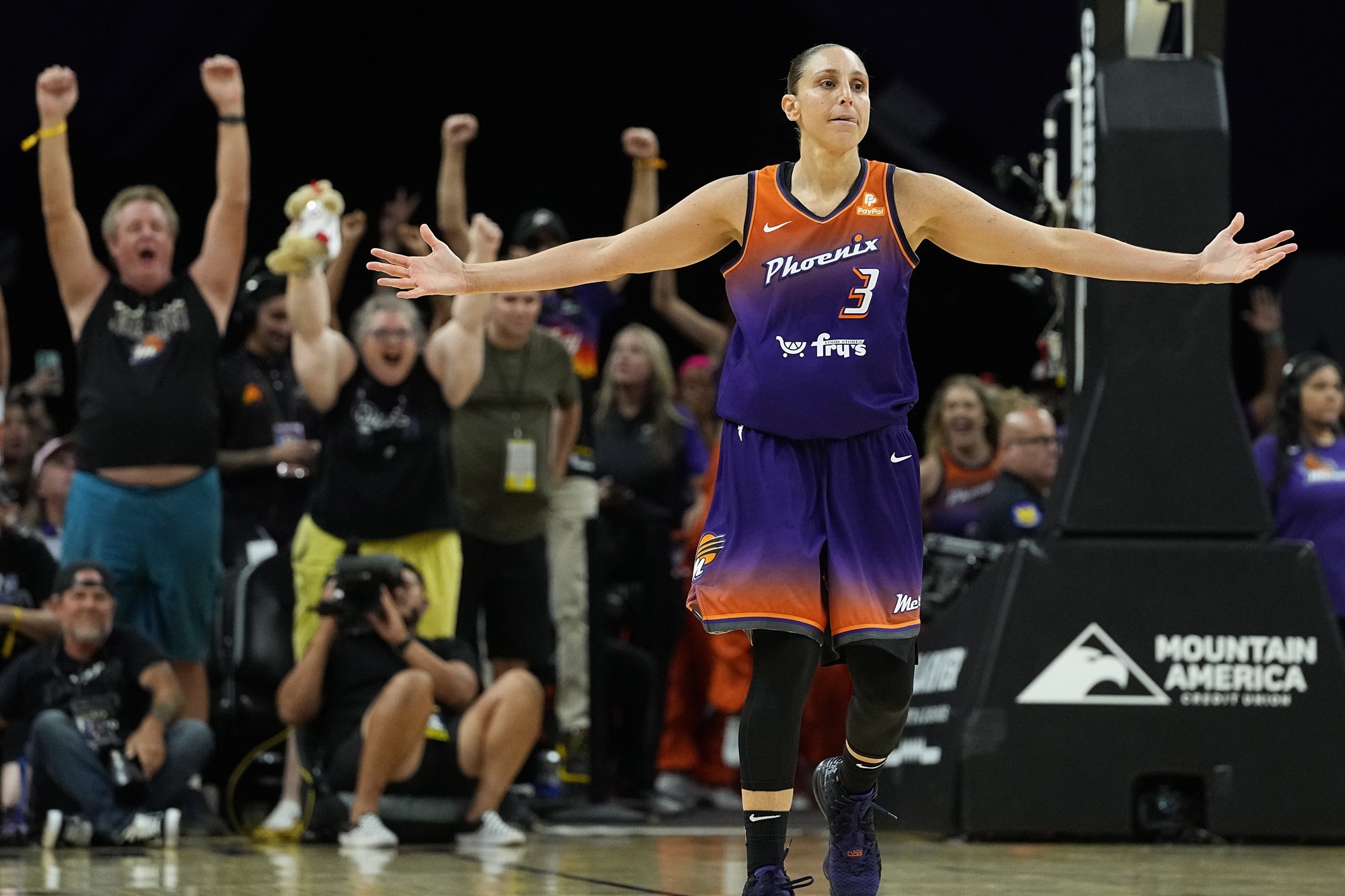 A female basketballer raises both arms in celebration during a game, with the crowd cheering on