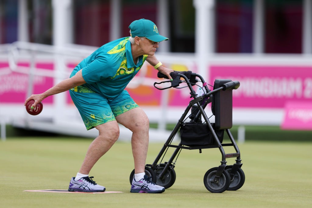 para-lawn bowler cheryl lindfield prepares to launch a ball while holding onto a walker