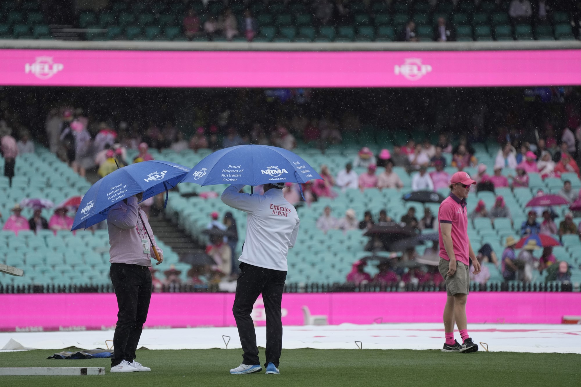 Umpires stand under umbrellas at the SCG where the pitch is covered.