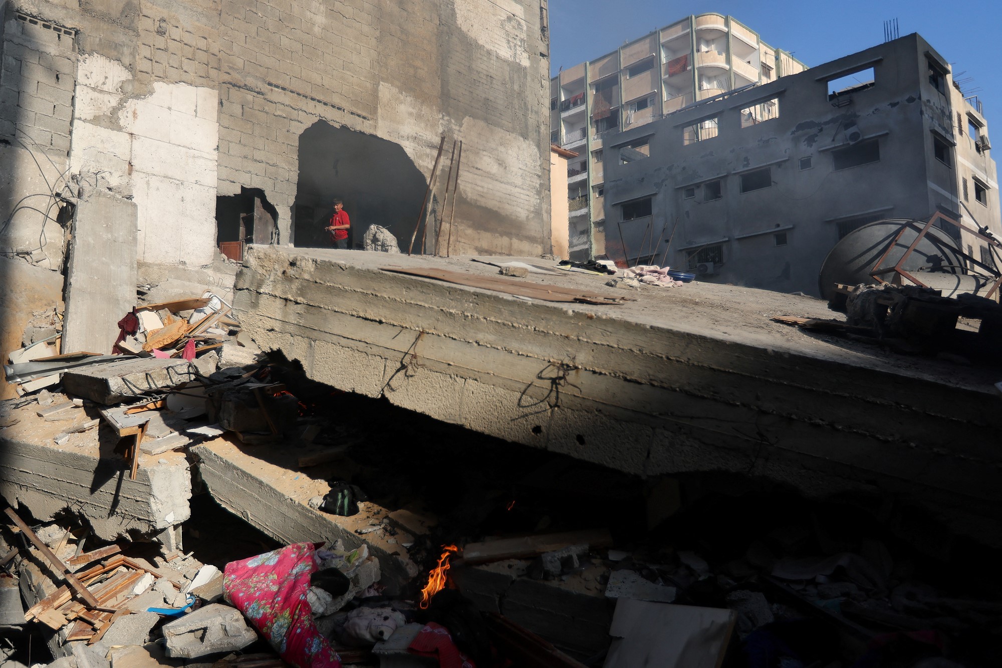 The side of a building with a wall collapsed and a child standing in the distance.
