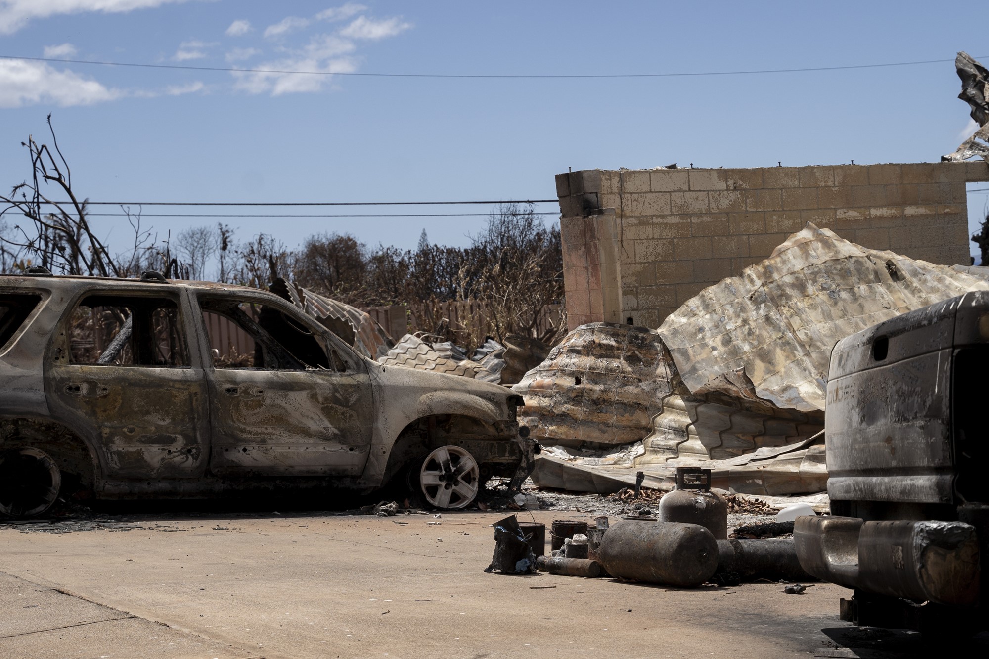 A burnt out car next to a melted tin roof.