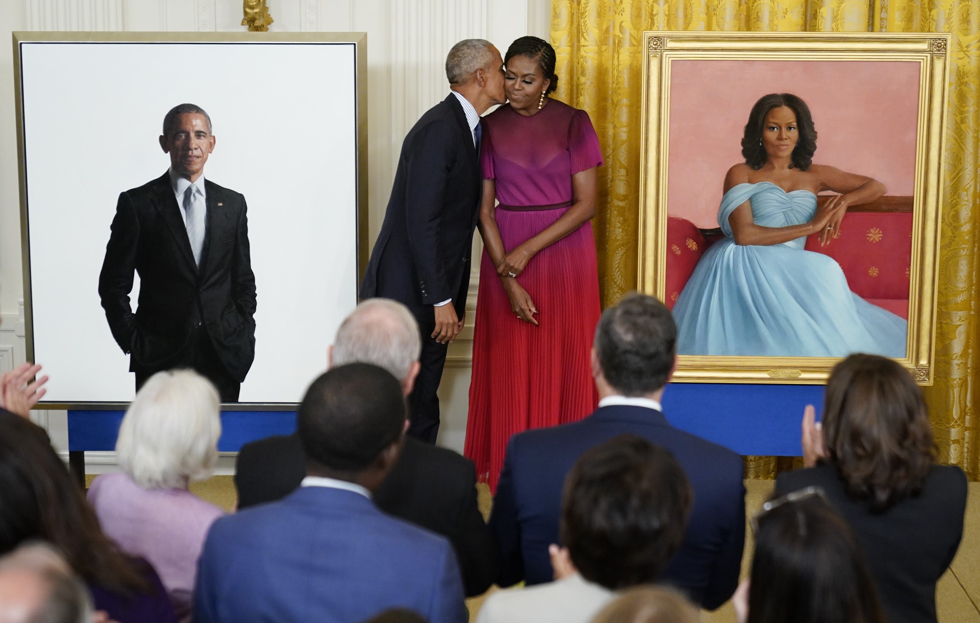 barack obama kisses wife michelle on the cheek standing between two portraits